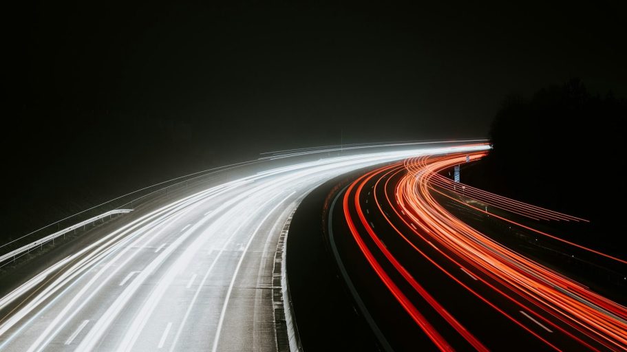 Mobility Langsame Lichtspuren von Fahrzeugen auf einer dunklen Straße, mit baumbewachsenen Ufern.